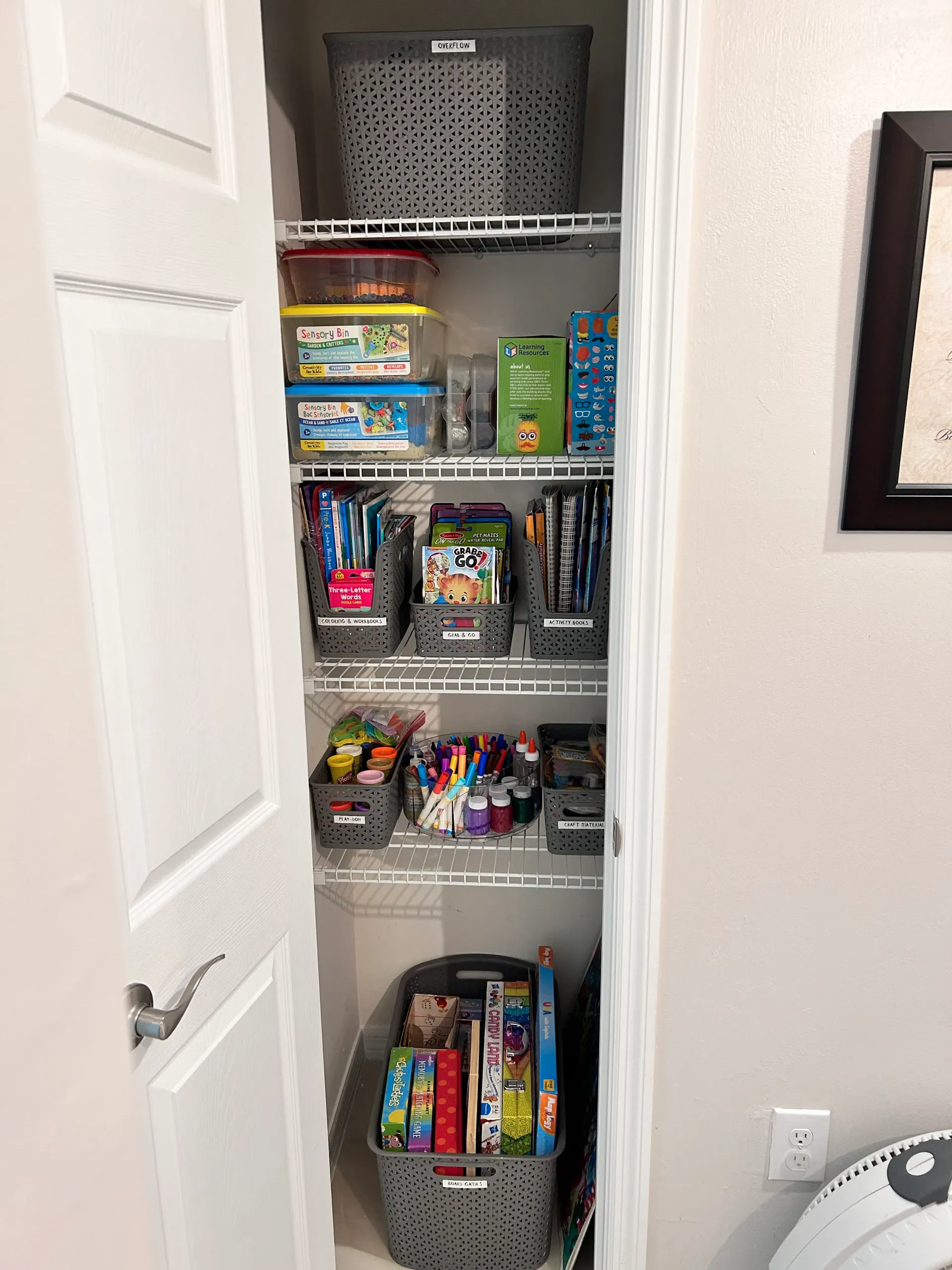 Organized play closet with labeled activity bins, books, craft supplies, and board games