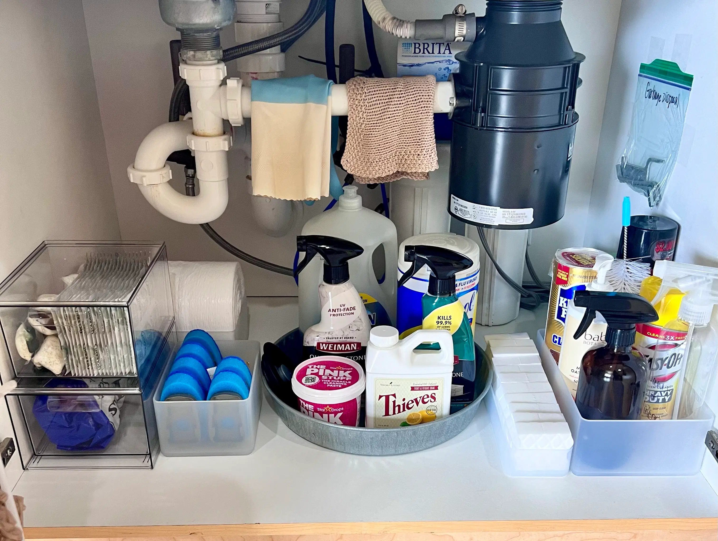 Organized under-sink cabinet with categorized cleaning supplies, a rotating tray, sponges, and cloths
