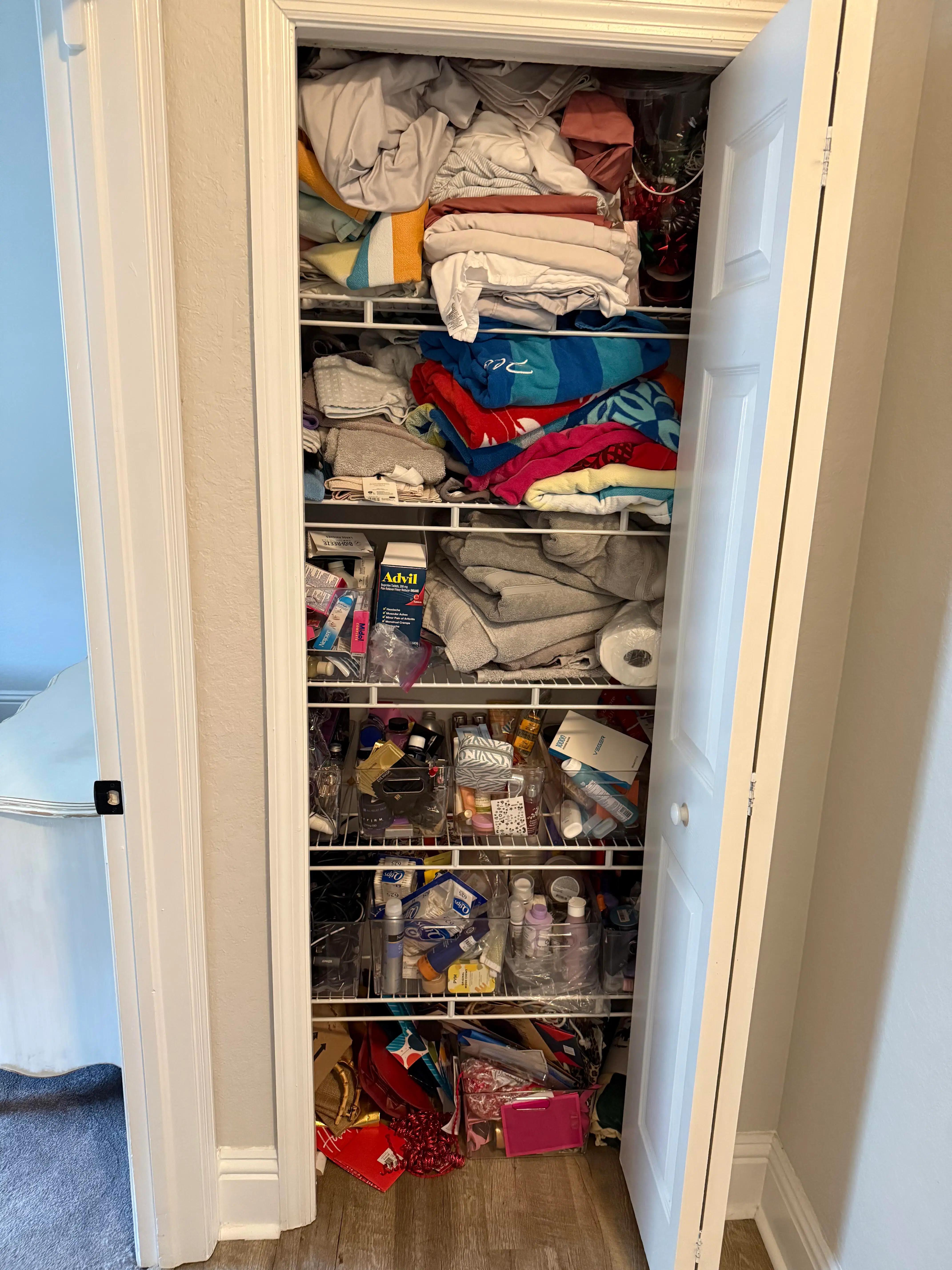 A linen closet with overflowing wire shelves holding mixed linens, towels, and toiletries before a Tidying Naples organizing session
