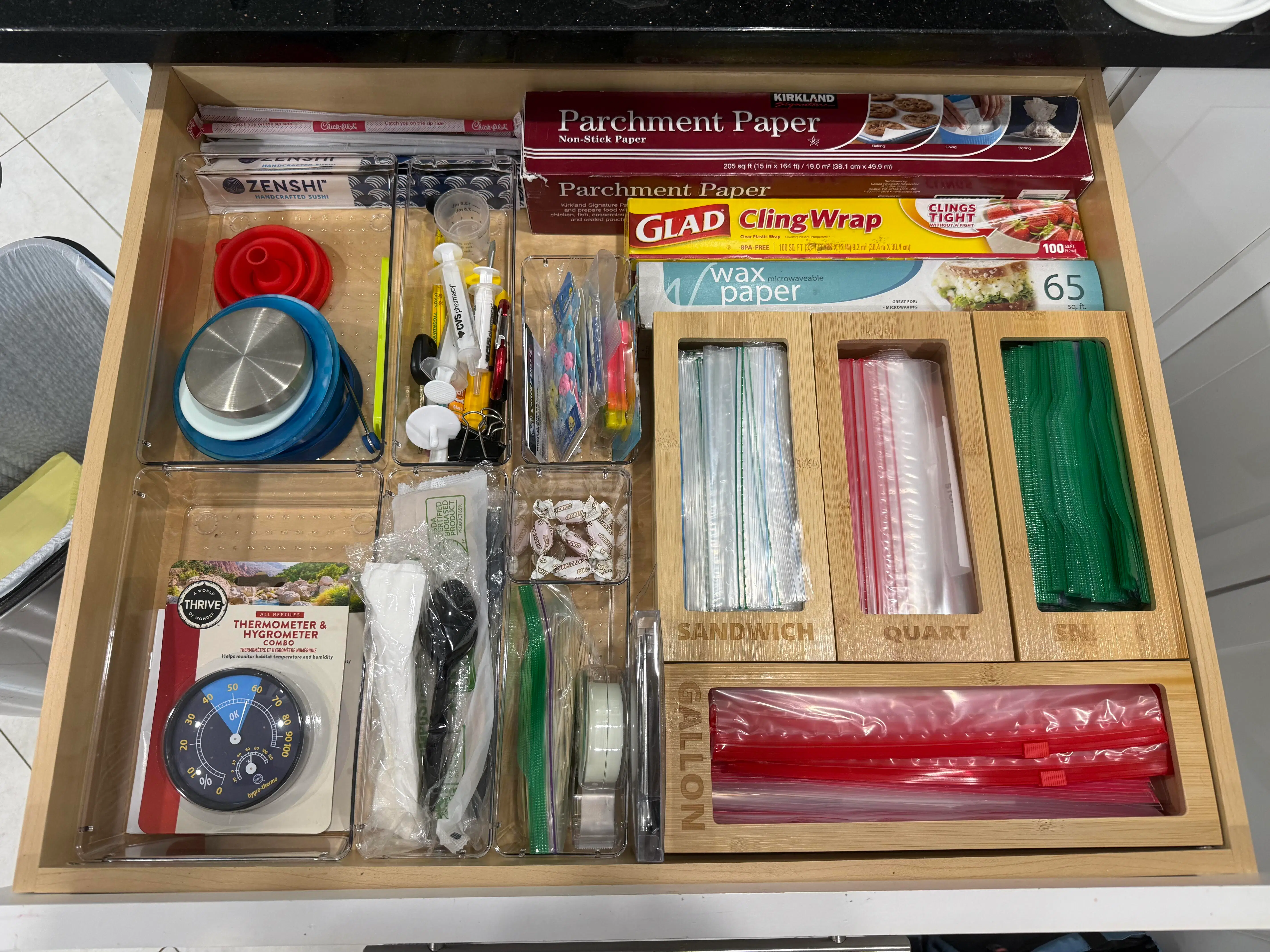 A kitchen utility drawer with food wraps, bags, clips, and kitchen tools arranged in divided sections for easier access and restocking