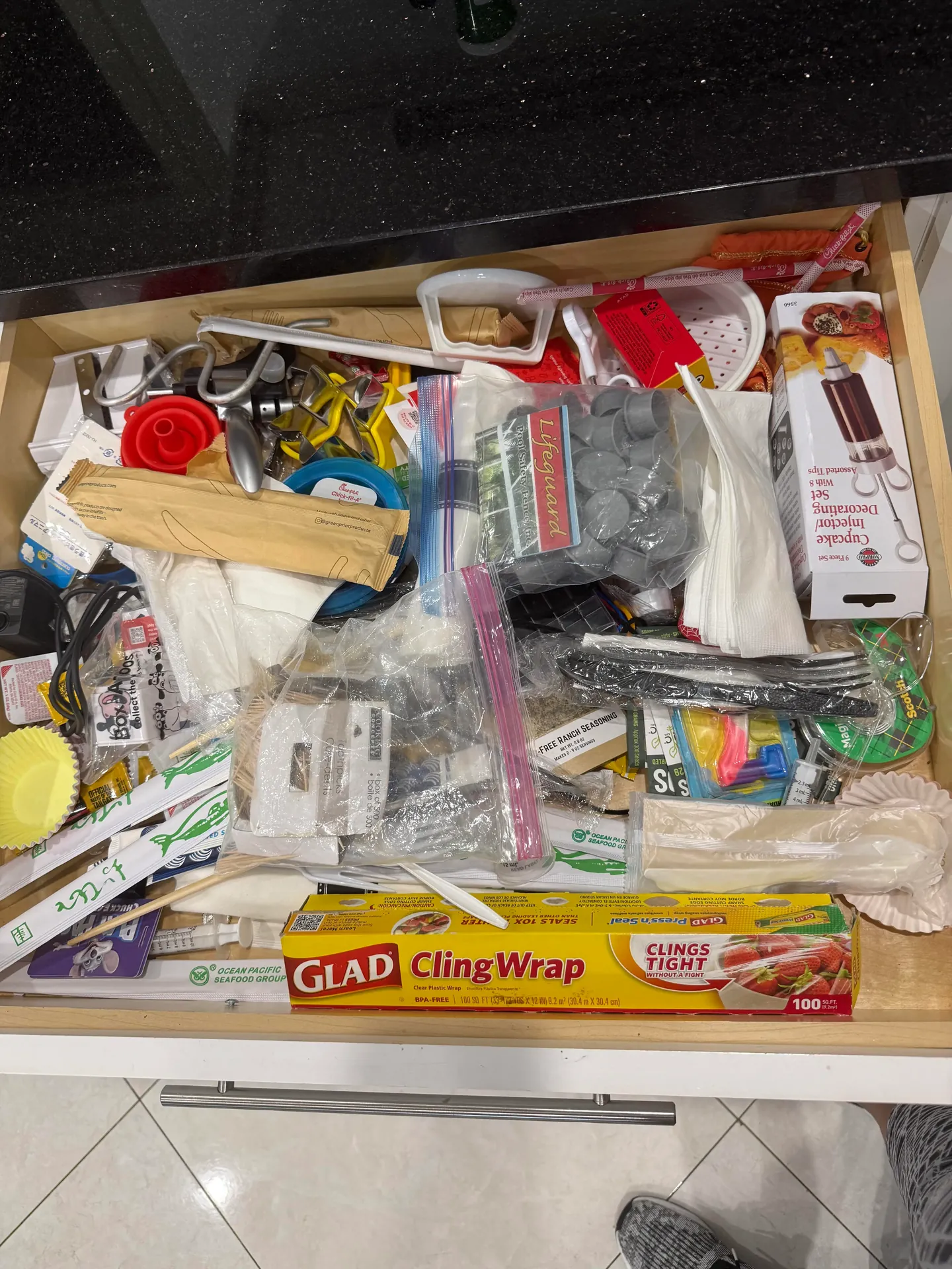 A kitchen utility drawer with food wraps, clips, small tools, and household items mixed together before organizing