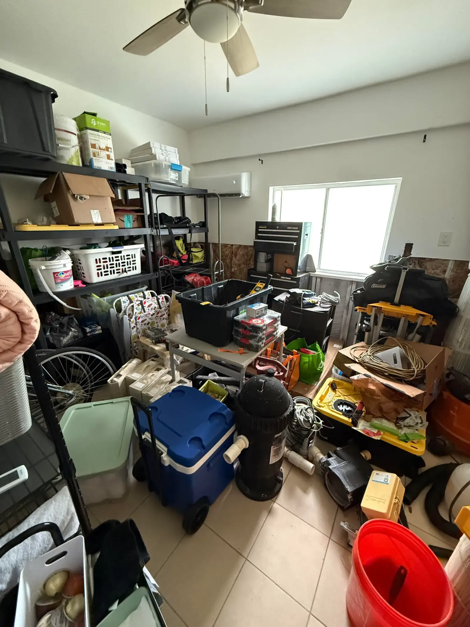 A utility and storage room with tools, containers, equipment, and household supplies gathered across shelves and the floor