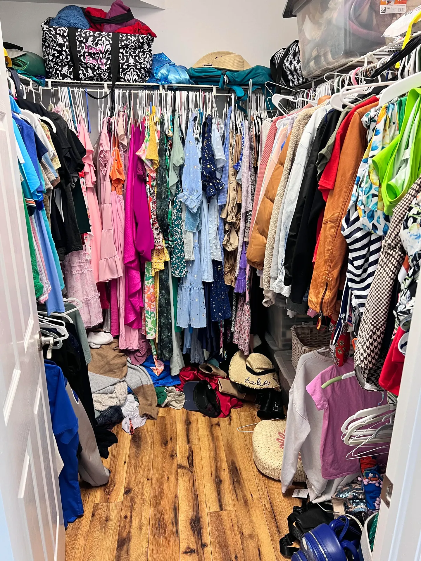 A walk-in closet with colorful clothes packed closely together, bags and folded items on the floor, before a Tidying Naples organizing session