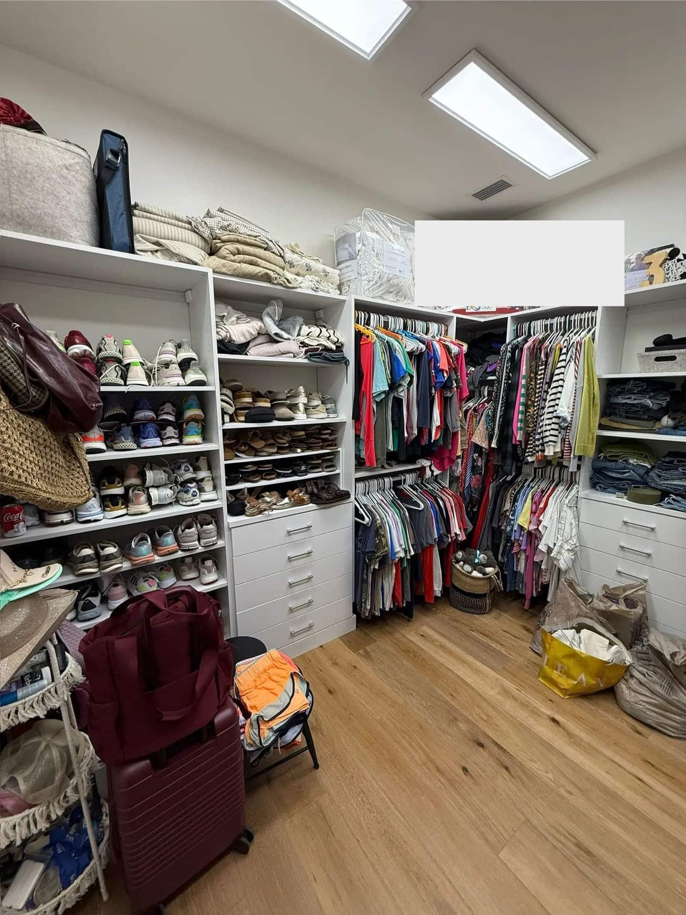 A walk-in closet with shoes, folded clothing, hanging clothes, and bags arranged across the shelves and floor